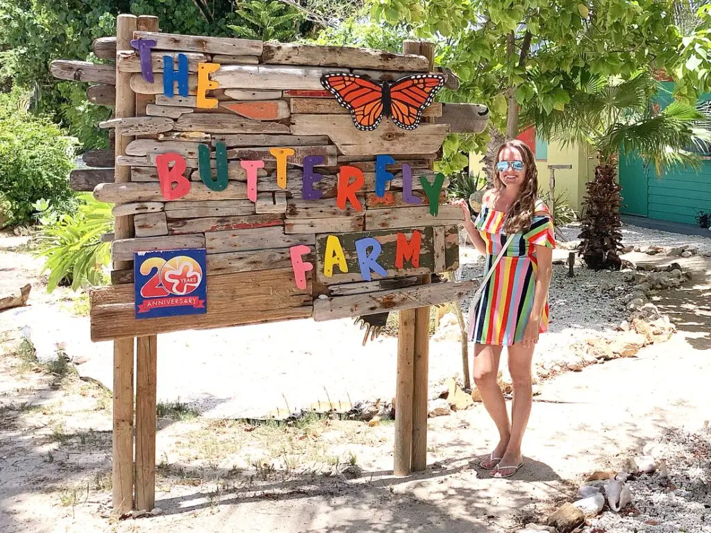 woman wearing striped multicolored dress standing beside Aruba Butterfly Farm sign