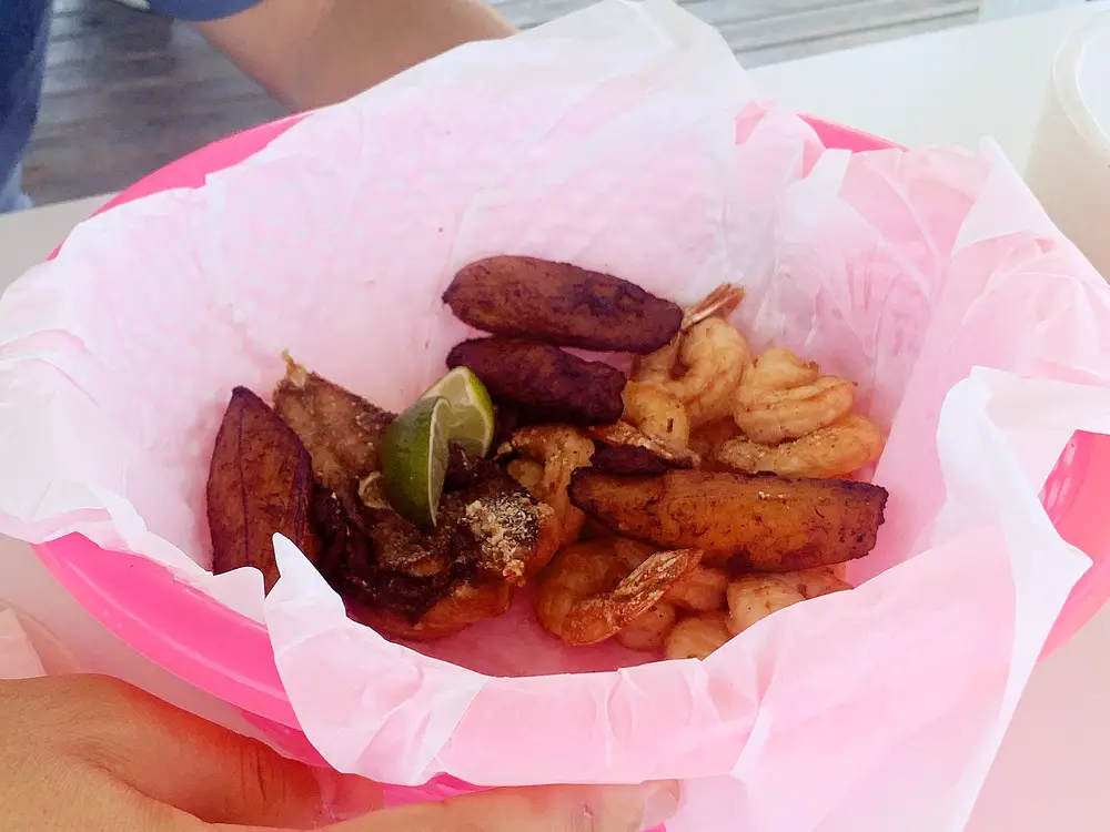 pink basket containing fried plantains, grilled shrimp, and lime wedges at Zeerover Restaurant in Aruba