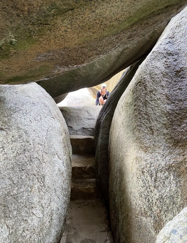 woman kneeling at the entrance to a narrow rock passageway at the Ayo Rock Formations in Aruba