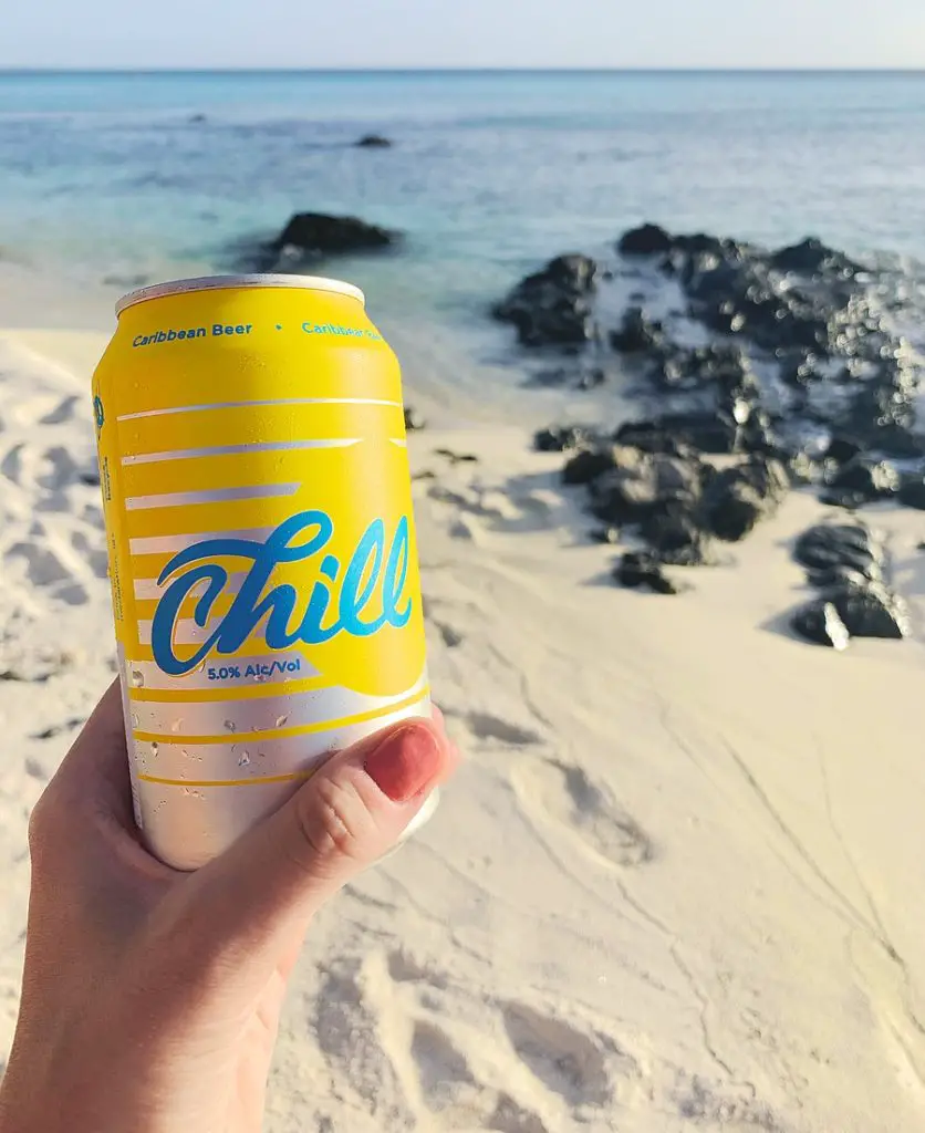a yellow and blue can of Balashi Chill beer on a sandy beach in Aruba