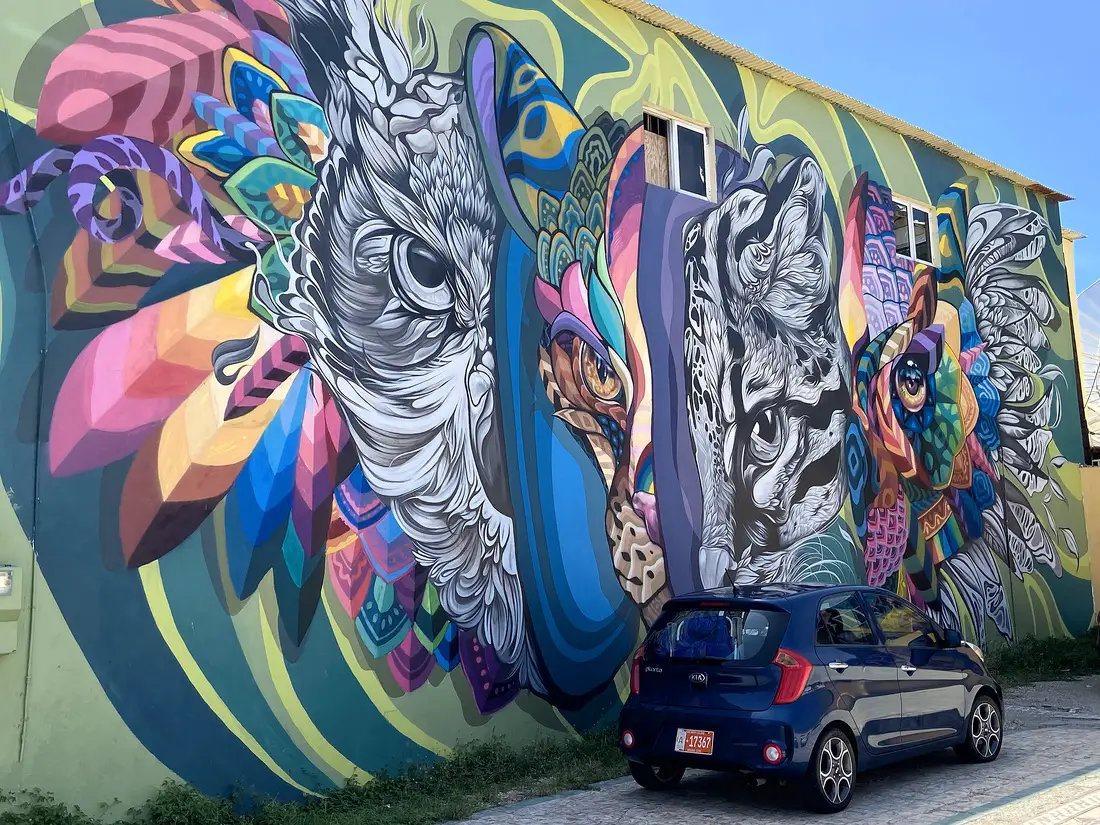 blue car parked beside a colorful street mural in San Nicolas, Aruba