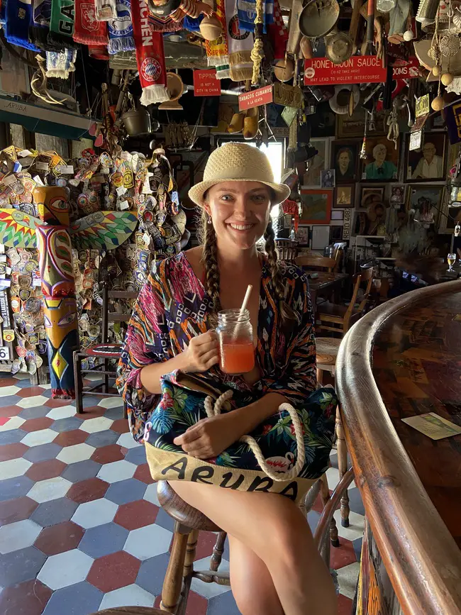 woman holding a “Boozer Colada” cocktail while sitting in Charlie’s Bar in San Nicolas, Aruba
