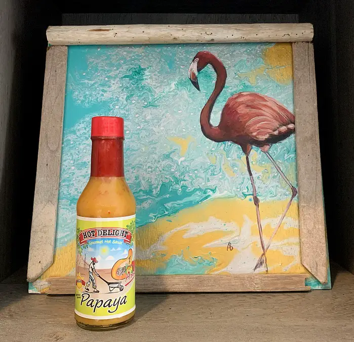 a bottle of Hot Delight Papaya Hot Sauce in front of a painting of a flamingo