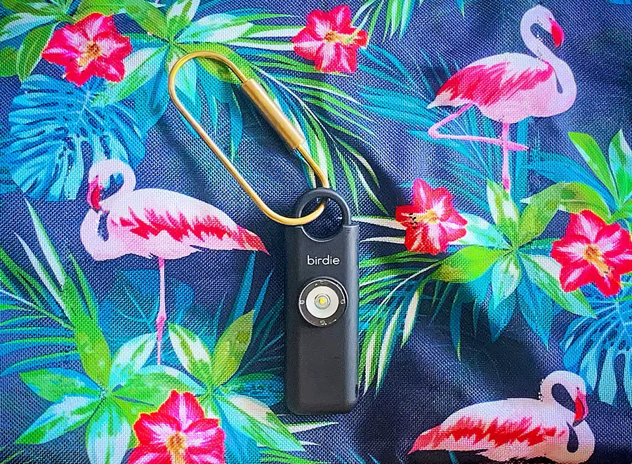 a Birdie personal safety alarm lying on a piece of tropical-looking fabric featuring flamingos