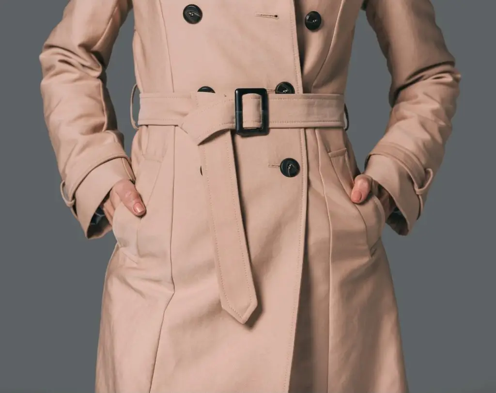 a woman wearing a khaki trench coat with her hands in her pockets